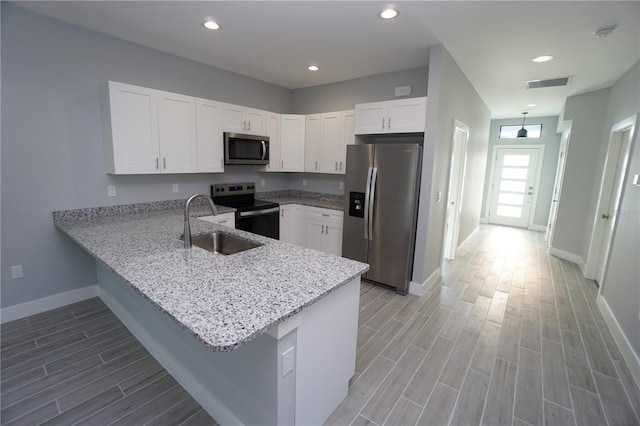 kitchen with kitchen peninsula, white cabinets, stainless steel appliances, and light hardwood / wood-style floors