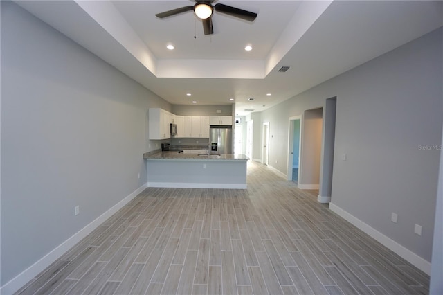 kitchen featuring a tray ceiling, light wood-style flooring, a peninsula, appliances with stainless steel finishes, and white cabinetry