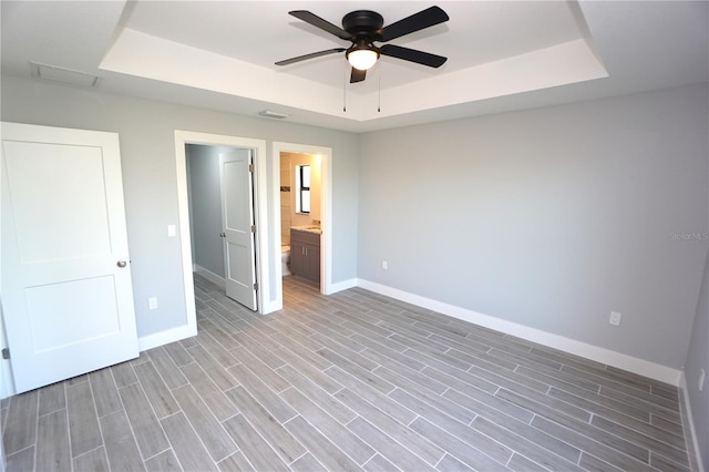 unfurnished bedroom featuring ensuite bathroom, ceiling fan, a raised ceiling, and light wood-type flooring