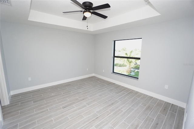 spare room with ceiling fan, a raised ceiling, and light wood-type flooring