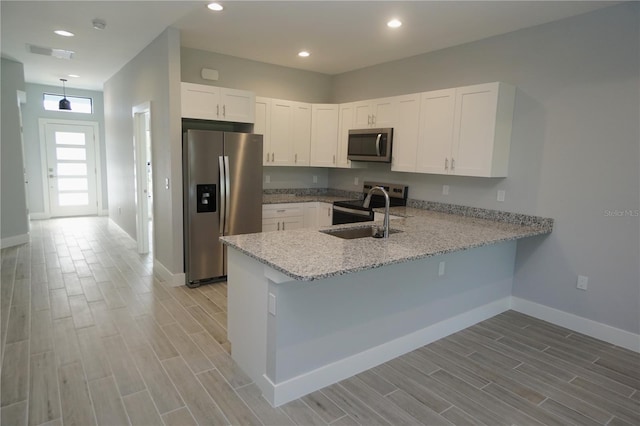 kitchen featuring a peninsula, stainless steel appliances, wood finish floors, and a sink