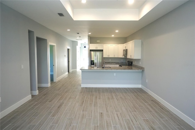 kitchen featuring light stone countertops, light wood finished floors, a peninsula, a sink, and stainless steel appliances