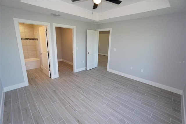 unfurnished bedroom with a ceiling fan, baseboards, visible vents, wood finish floors, and a tray ceiling