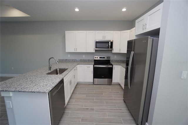 kitchen featuring a sink, appliances with stainless steel finishes, a peninsula, white cabinets, and light stone countertops