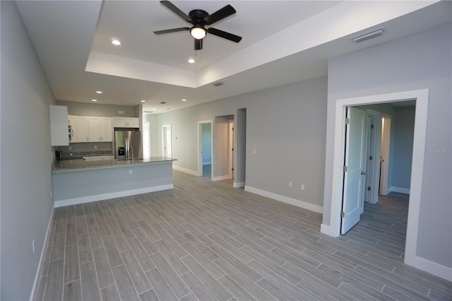 unfurnished living room featuring wood finish floors, recessed lighting, baseboards, and a tray ceiling