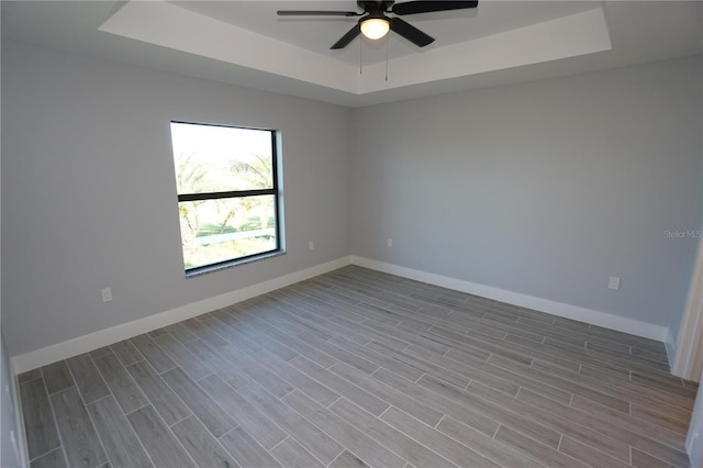 spare room with a tray ceiling, a ceiling fan, baseboards, and wood tiled floor