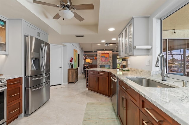 kitchen featuring light stone counters, stainless steel appliances, a raised ceiling, and sink