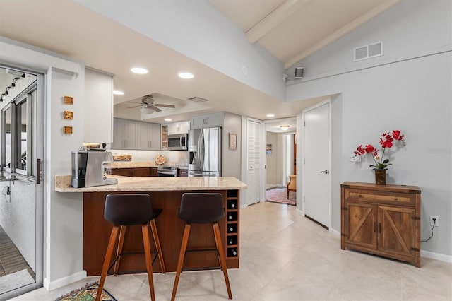 kitchen with lofted ceiling, a breakfast bar area, gray cabinetry, kitchen peninsula, and stainless steel appliances