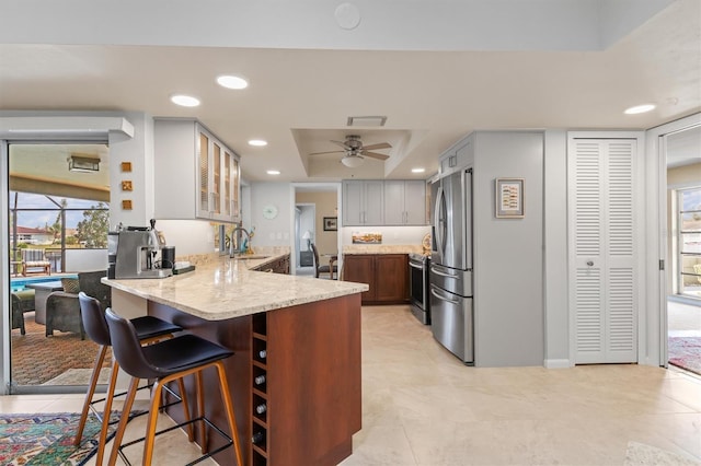 kitchen featuring appliances with stainless steel finishes, sink, kitchen peninsula, a raised ceiling, and light stone countertops