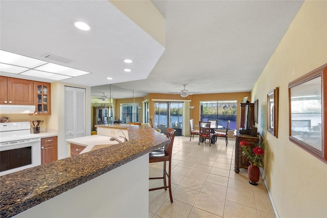 kitchen with pendant lighting, electric stove, sink, ceiling fan, and a breakfast bar area