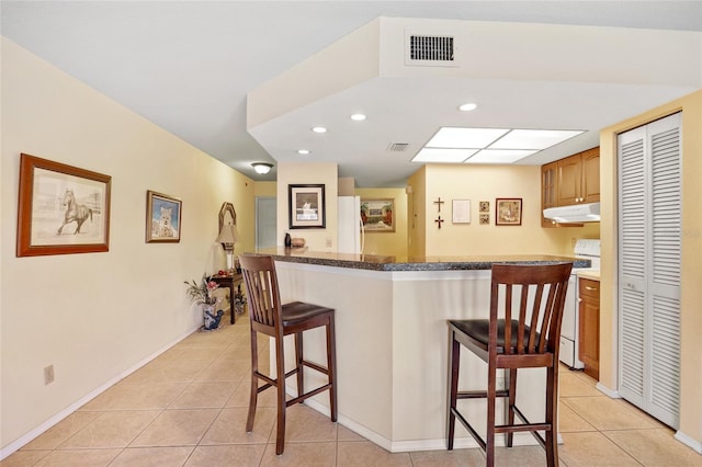 kitchen with a center island, a breakfast bar, light tile patterned flooring, and white appliances