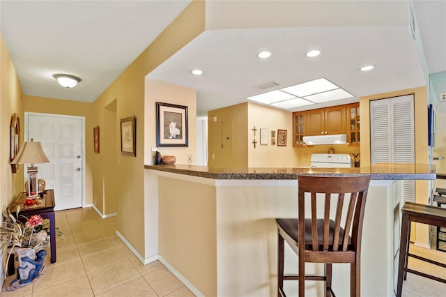 kitchen featuring a breakfast bar, range, kitchen peninsula, and light tile patterned flooring