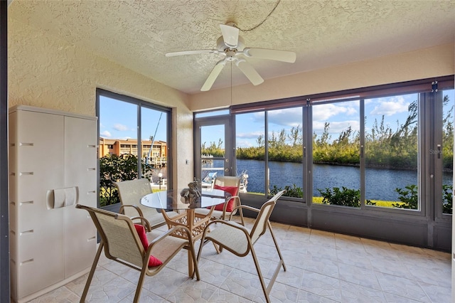 sunroom with ceiling fan and a water view