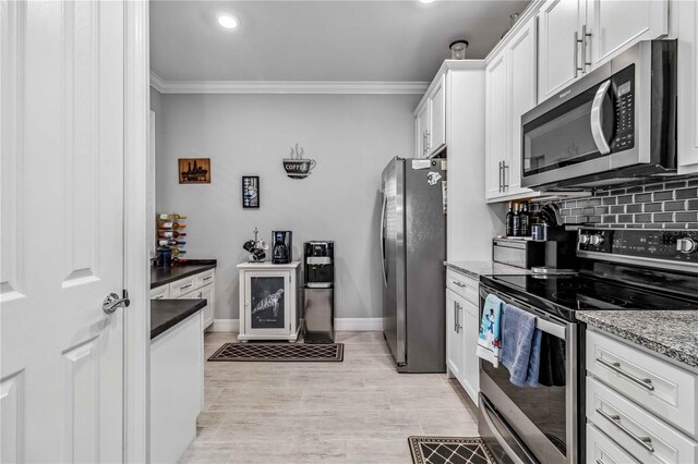 kitchen with dark stone countertops, crown molding, white cabinetry, and stainless steel appliances