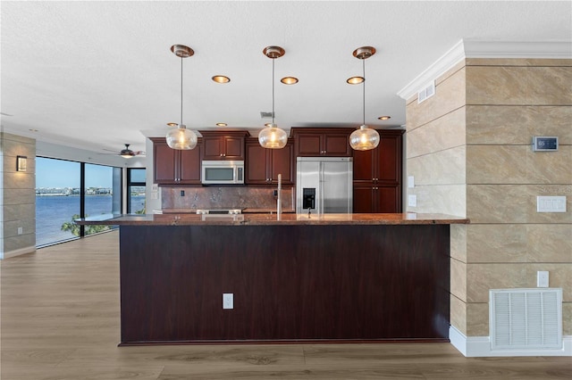 kitchen featuring a water view, light wood-type flooring, decorative light fixtures, and appliances with stainless steel finishes