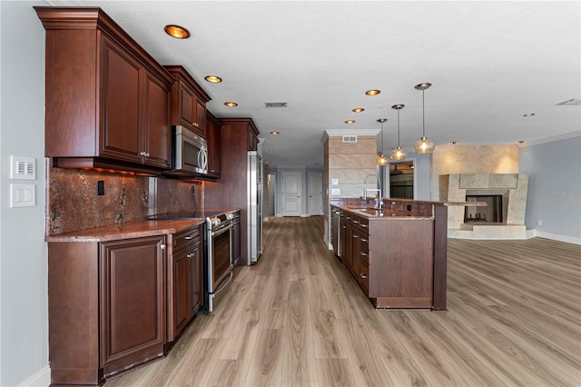 kitchen featuring stainless steel appliances, a stone fireplace, light hardwood / wood-style floors, decorative light fixtures, and dark brown cabinets