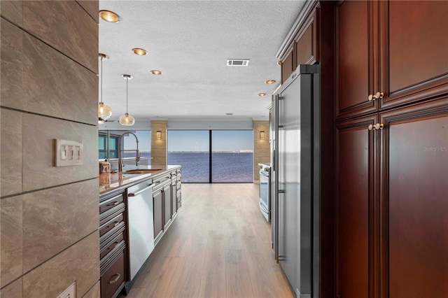 kitchen with pendant lighting, a water view, sink, light wood-type flooring, and appliances with stainless steel finishes