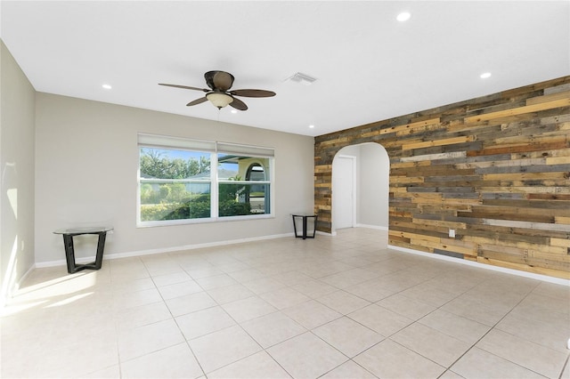 unfurnished living room featuring ceiling fan, light tile patterned floors, and wood walls