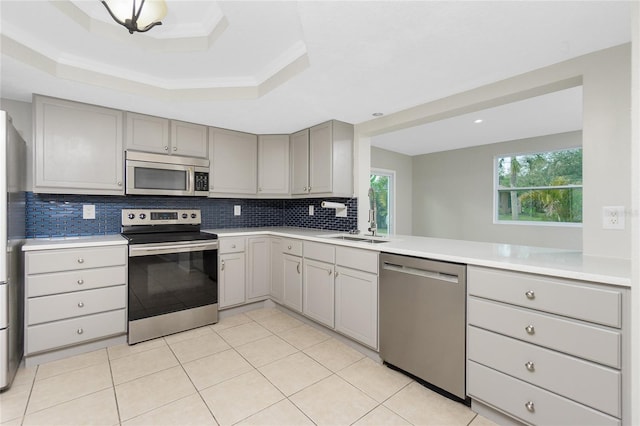 kitchen with stainless steel appliances, a raised ceiling, kitchen peninsula, and gray cabinetry