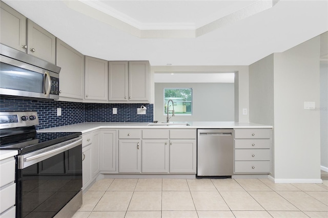 kitchen featuring sink, gray cabinets, appliances with stainless steel finishes, decorative backsplash, and a raised ceiling