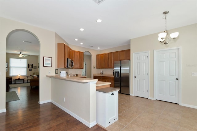 kitchen with kitchen peninsula, decorative light fixtures, light tile patterned floors, ceiling fan with notable chandelier, and appliances with stainless steel finishes