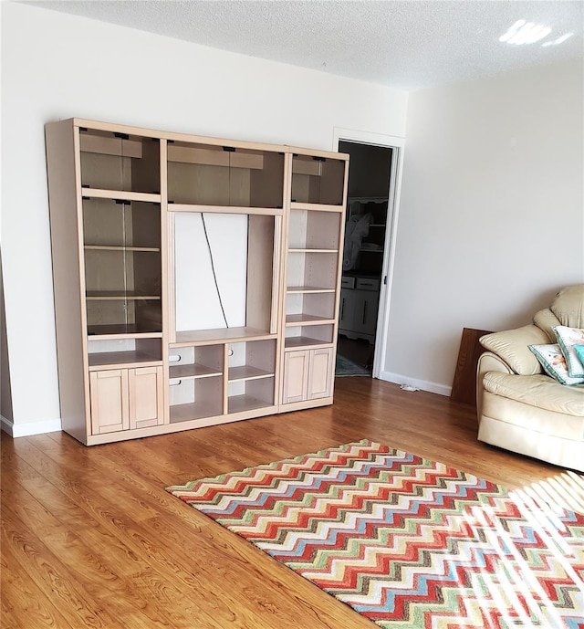 unfurnished living room featuring wood finished floors, baseboards, and a textured ceiling