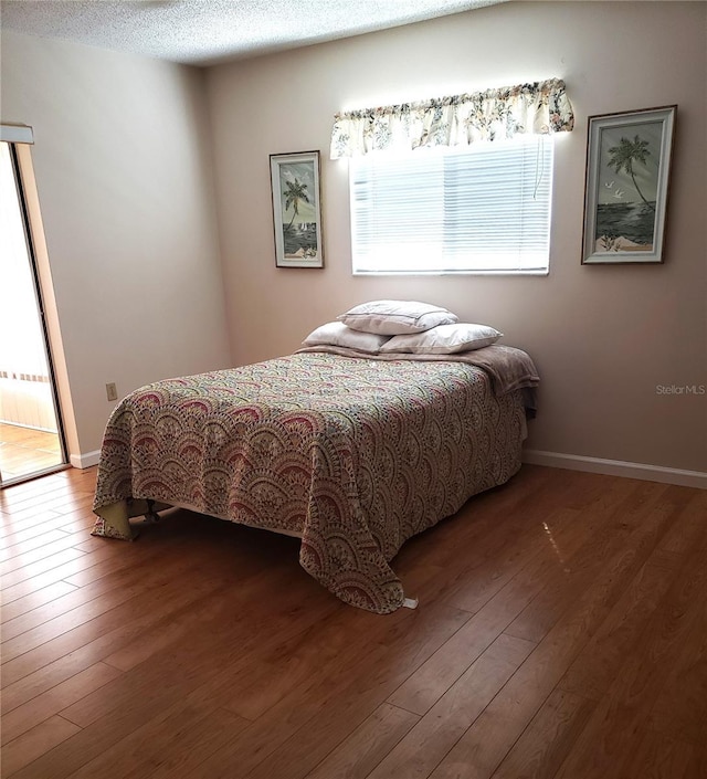 bedroom with wood-type flooring, a textured ceiling, and baseboards