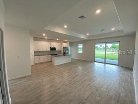 unfurnished living room with light hardwood / wood-style floors and a raised ceiling