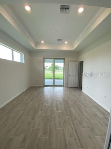 empty room with a raised ceiling, crown molding, plenty of natural light, and hardwood / wood-style floors