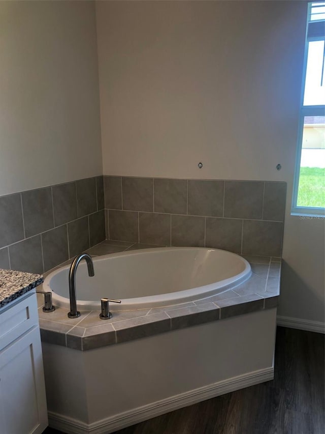 bathroom with hardwood / wood-style flooring, vanity, and a relaxing tiled tub