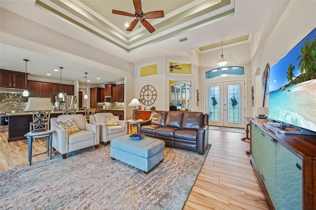 living room featuring ceiling fan, french doors, a high ceiling, crown molding, and light wood-type flooring