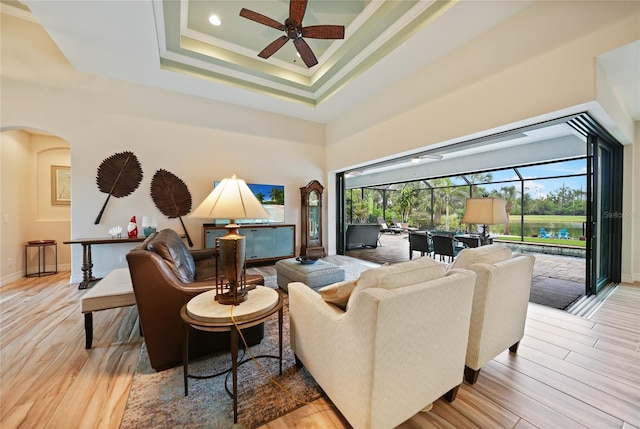 living room featuring ceiling fan, a towering ceiling, light wood-type flooring, a tray ceiling, and ornamental molding