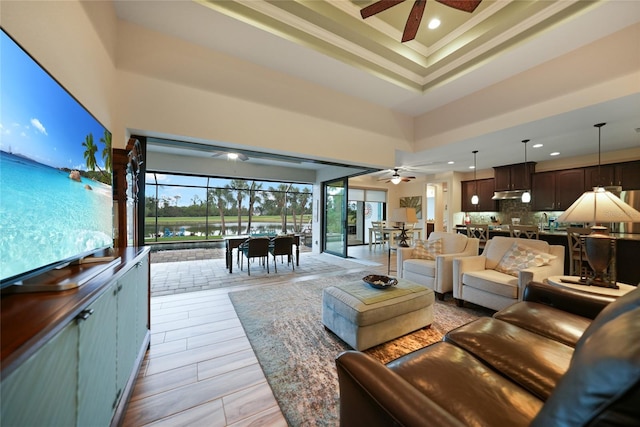 living room with ceiling fan, ornamental molding, a towering ceiling, and a tray ceiling