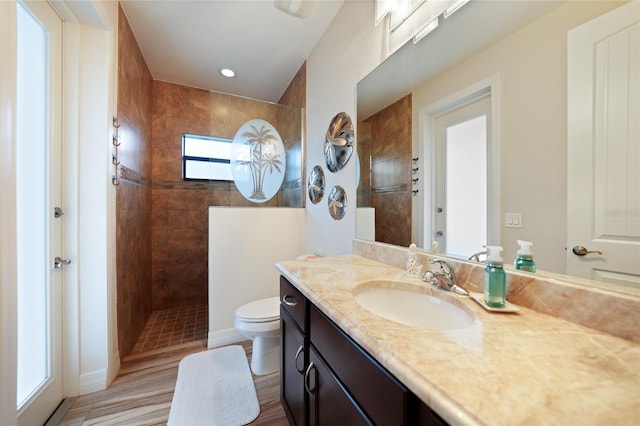 bathroom with hardwood / wood-style floors, vanity, toilet, and tiled shower