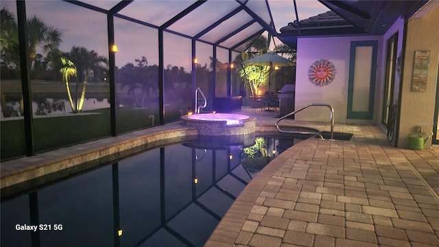 pool at dusk with glass enclosure, a patio area, and an in ground hot tub