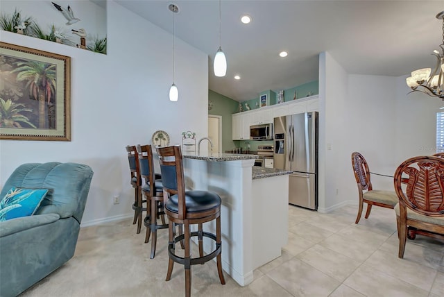 kitchen featuring stainless steel appliances, dark stone countertops, white cabinets, hanging light fixtures, and lofted ceiling