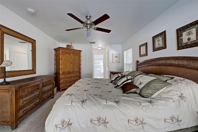 bedroom with ceiling fan, light colored carpet, and ensuite bath