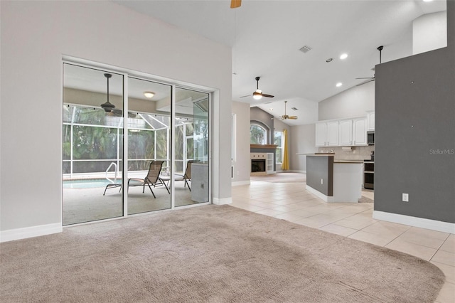 unfurnished living room with ceiling fan, light colored carpet, high vaulted ceiling, and a tiled fireplace