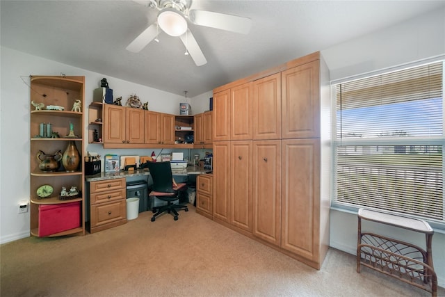 home office featuring built in desk, light colored carpet, and ceiling fan