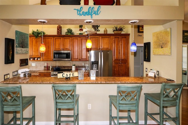 kitchen featuring decorative light fixtures, stone counters, kitchen peninsula, and appliances with stainless steel finishes