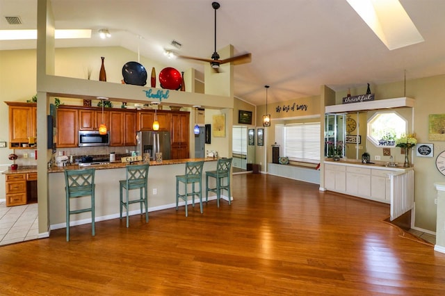 kitchen with kitchen peninsula, appliances with stainless steel finishes, hardwood / wood-style flooring, high vaulted ceiling, and decorative light fixtures