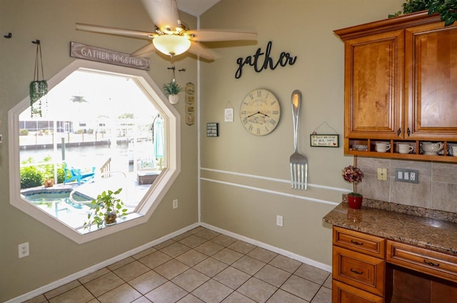 kitchen featuring ceiling fan, light stone counters, light tile patterned floors, and backsplash