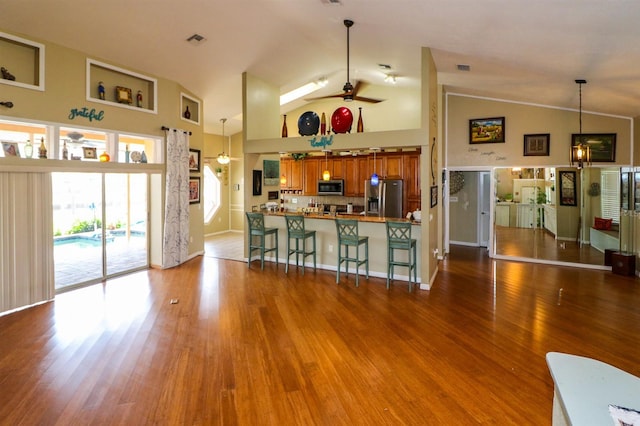 kitchen featuring hardwood / wood-style floors, pendant lighting, a breakfast bar area, ceiling fan with notable chandelier, and appliances with stainless steel finishes