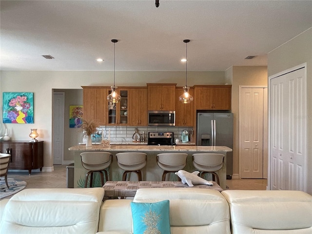 kitchen with decorative backsplash, stainless steel appliances, a kitchen bar, and hanging light fixtures