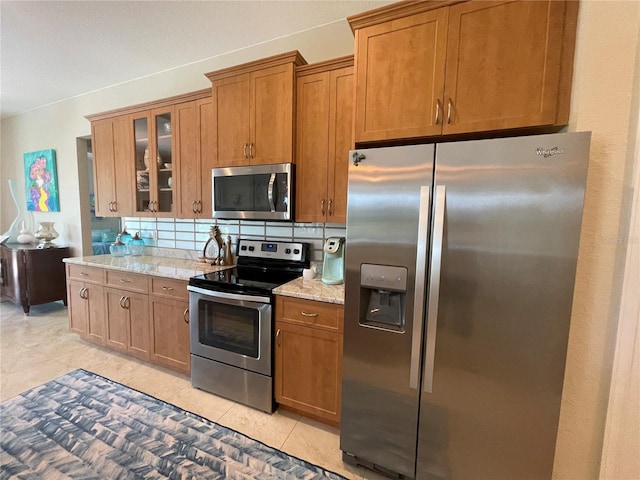 kitchen featuring light tile patterned flooring, appliances with stainless steel finishes, light stone counters, and decorative backsplash