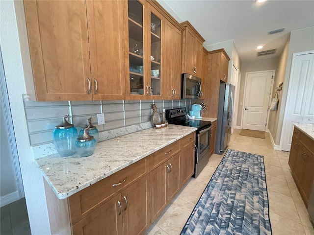 kitchen featuring stainless steel appliances, light tile patterned flooring, backsplash, and light stone counters