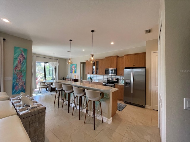 kitchen featuring tasteful backsplash, an island with sink, a kitchen breakfast bar, hanging light fixtures, and stainless steel appliances