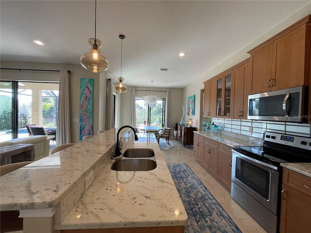 kitchen with sink, stainless steel appliances, an island with sink, and light stone countertops