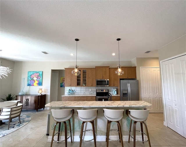 kitchen featuring appliances with stainless steel finishes, a kitchen bar, a kitchen island with sink, and hanging light fixtures