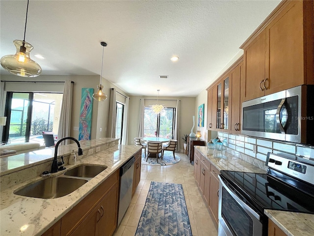 kitchen featuring sink, light stone counters, hanging light fixtures, light tile patterned floors, and appliances with stainless steel finishes